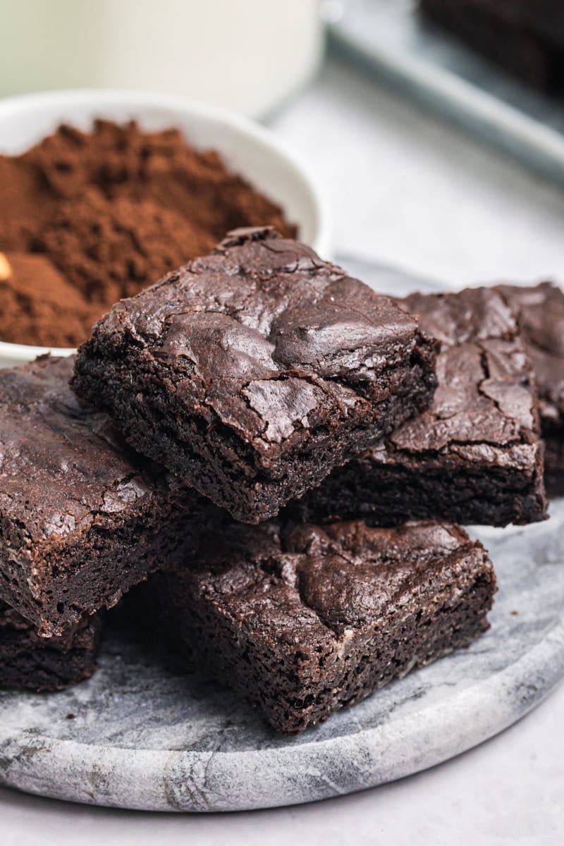 several dark cocoa brownies piled on a marble serving tray