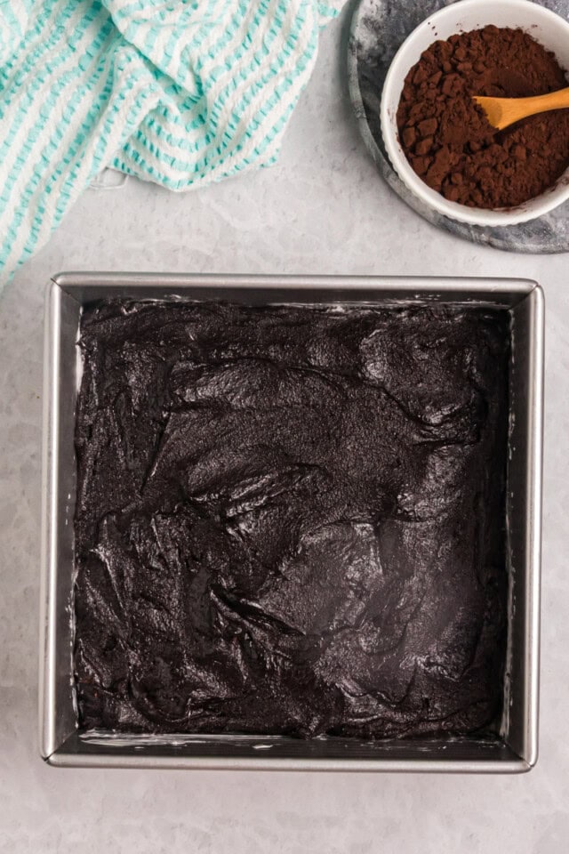overhead view of dark cocoa brownie batter spread in a square baking pan ready to go into the oven