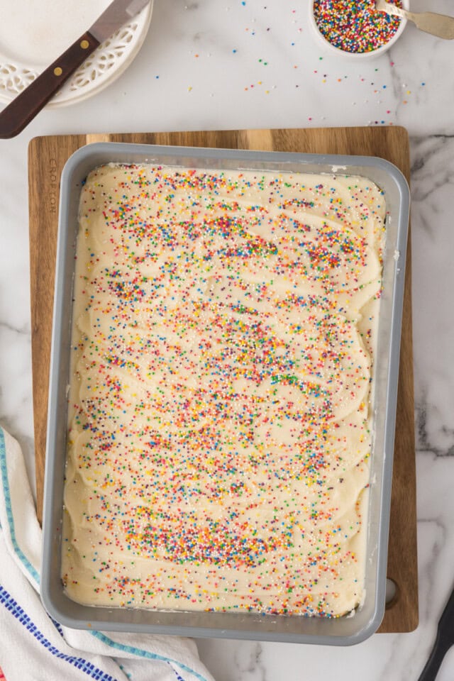overhead view of frosted sugar cookie bars topped with rainbow sprinkles in a 9x13 baking pan