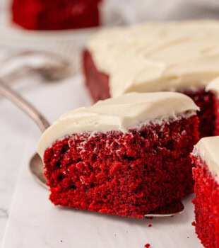 a slice of red velvet sheet cake on a cake server being removed from the remaining cake
