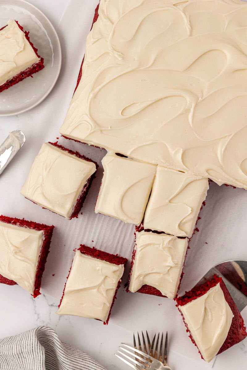 red velvet sheet cake with cream cheese frosting partially sliced into squares