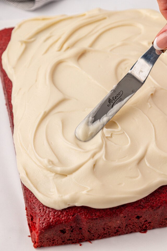 cream cheese frosting being spread over red velvet sheet cake