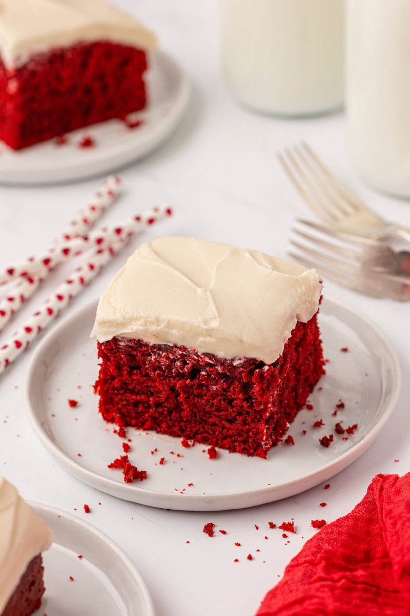 a slice of red velvet sheet cake with cream cheese frosting on a white plate