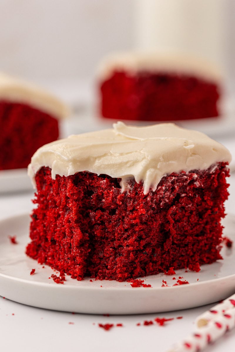 a slice of red velvet sheet cake with cream cheese frosting with a bite missing from the front corner