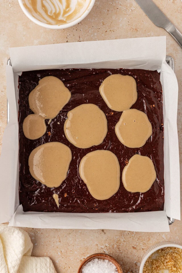 overhead view of tahini dolloped over brownie batter in a square baking pan