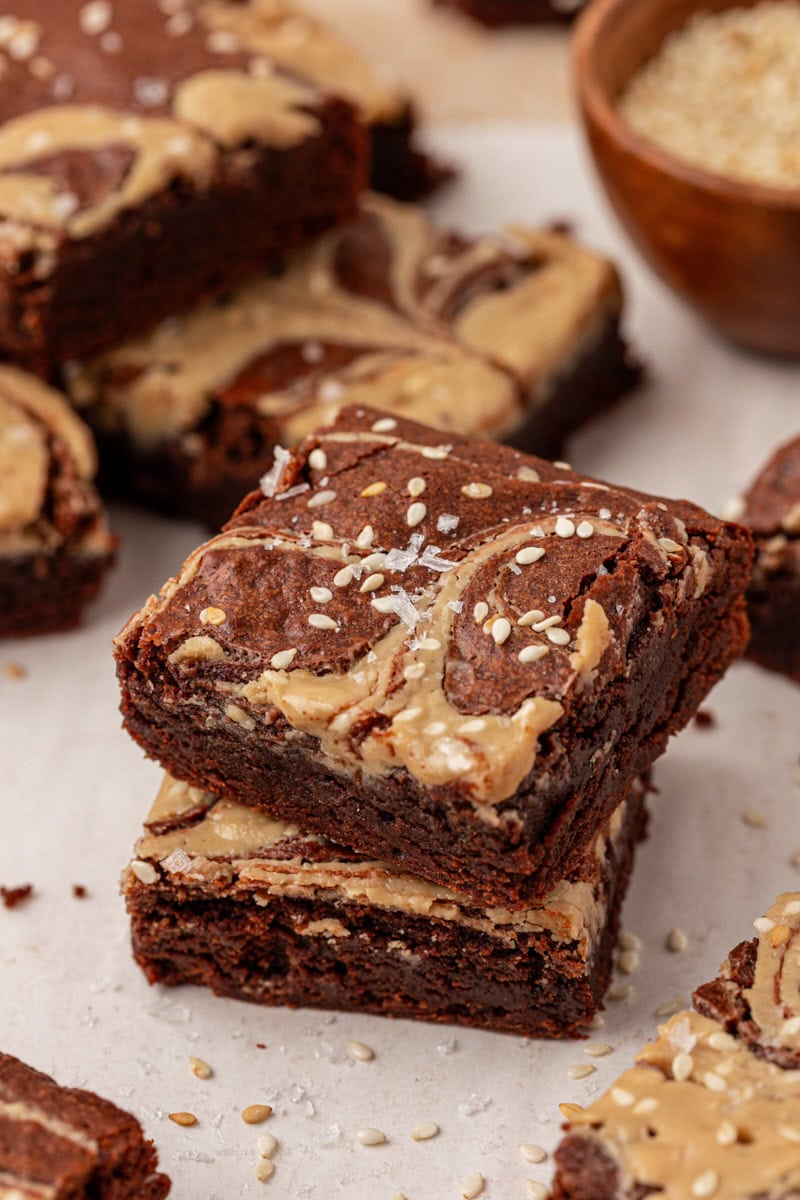 a stack of two tahini brownies on parchment paper surrounded by more brownies