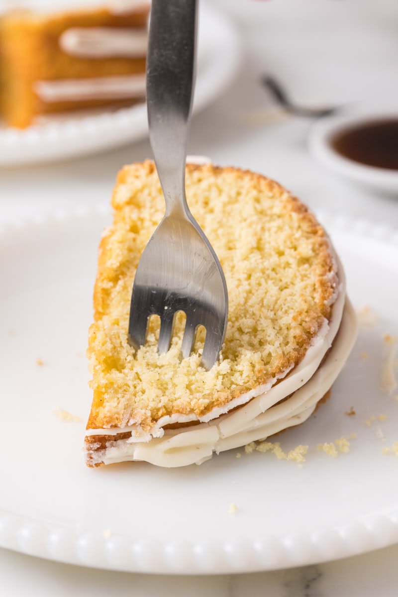 a fork cutting into a slice of vanilla Bundt cake on a white plate
