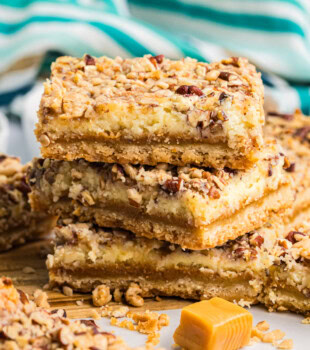 stack of three caramel cheesecake bars with layers of buttery crust, caramel, cheesecake, and crunchy topping