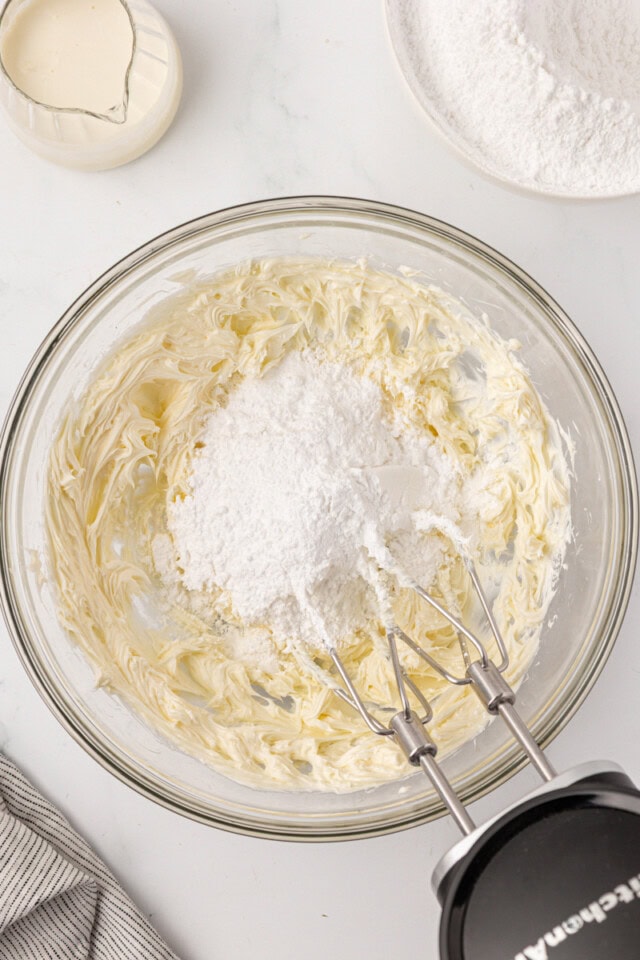 overhead view of confectioners' sugar added to creamed butter in a glass mixing bowl
