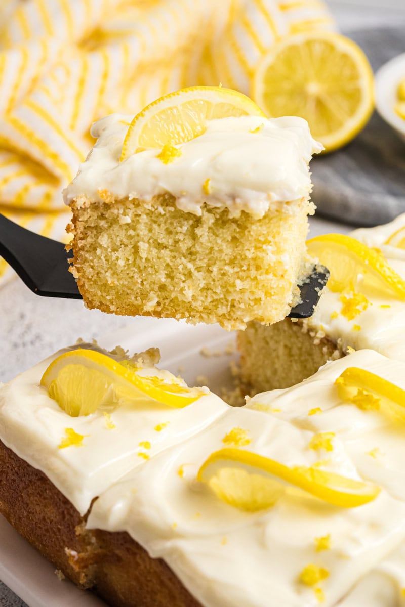 a slice of lemon sheet cake on a cake server lifting away from the remaining cake