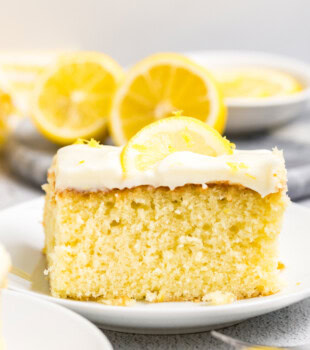 a slice of lemon sheet cake with lemon cream cheese frosting topped with lemon slices and zest