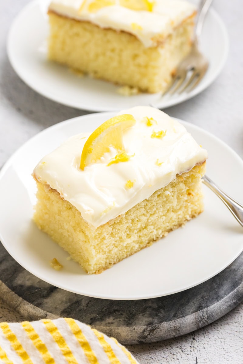 a slice of lemon sheet cake with lemon cream cheese frosting on a white plate
