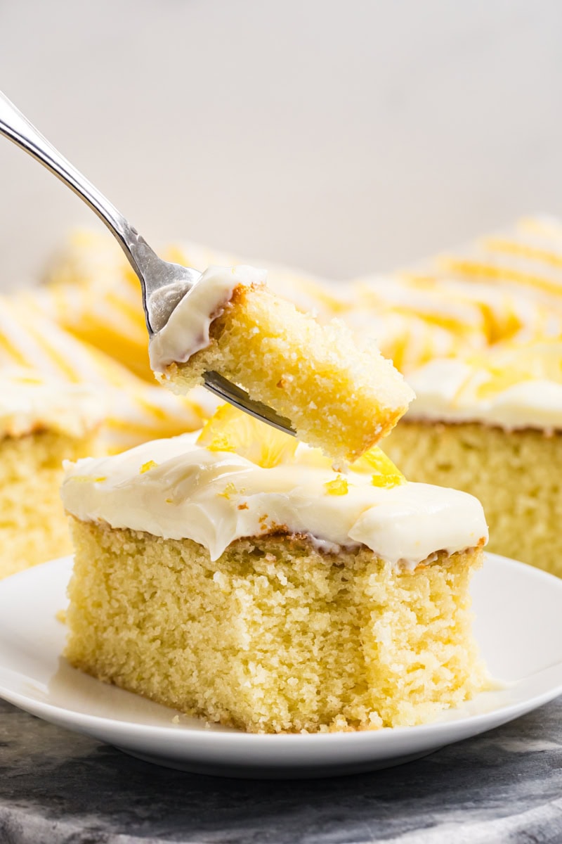a bite of lemon sheet cake on a fork with the remaining slice of cake