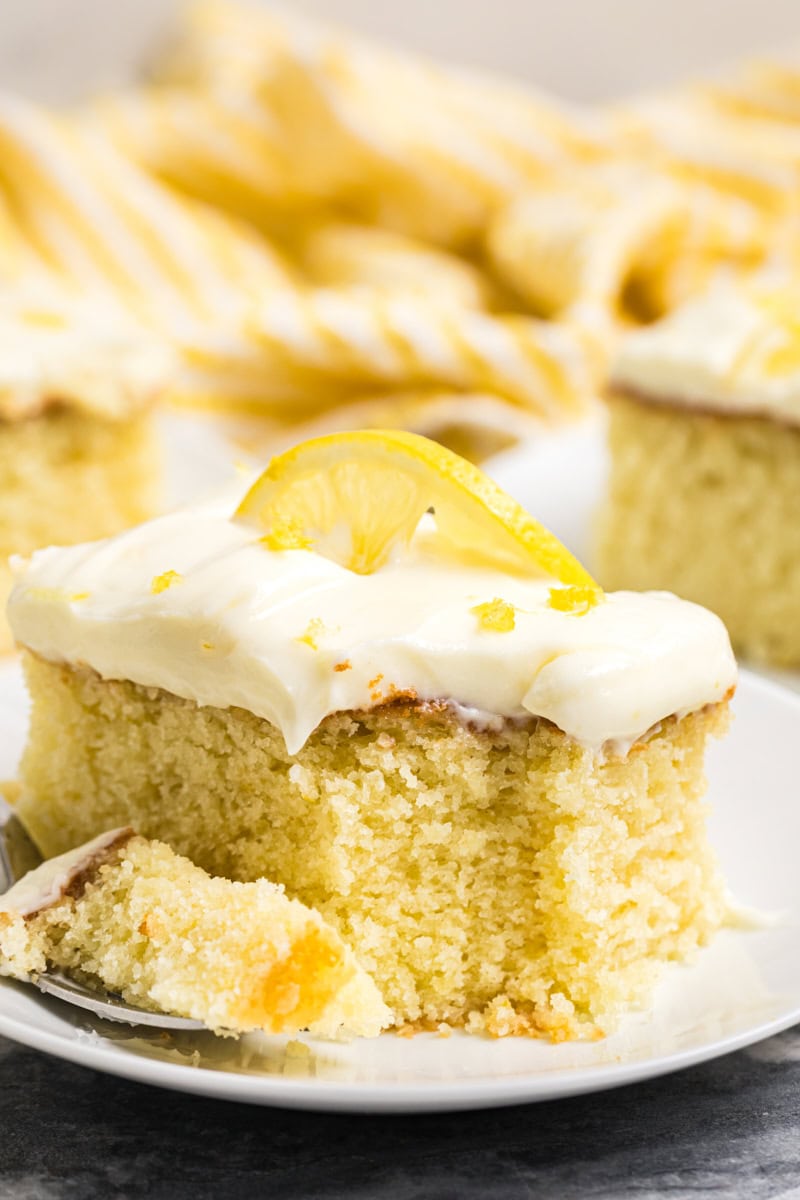close up of a slice of lemon sheet cake topped with a lemon slice and zest