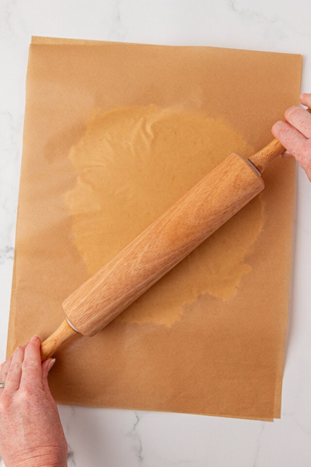 overhead view of lemon shortbread cookie dough being rolled between sheets of parchment paper