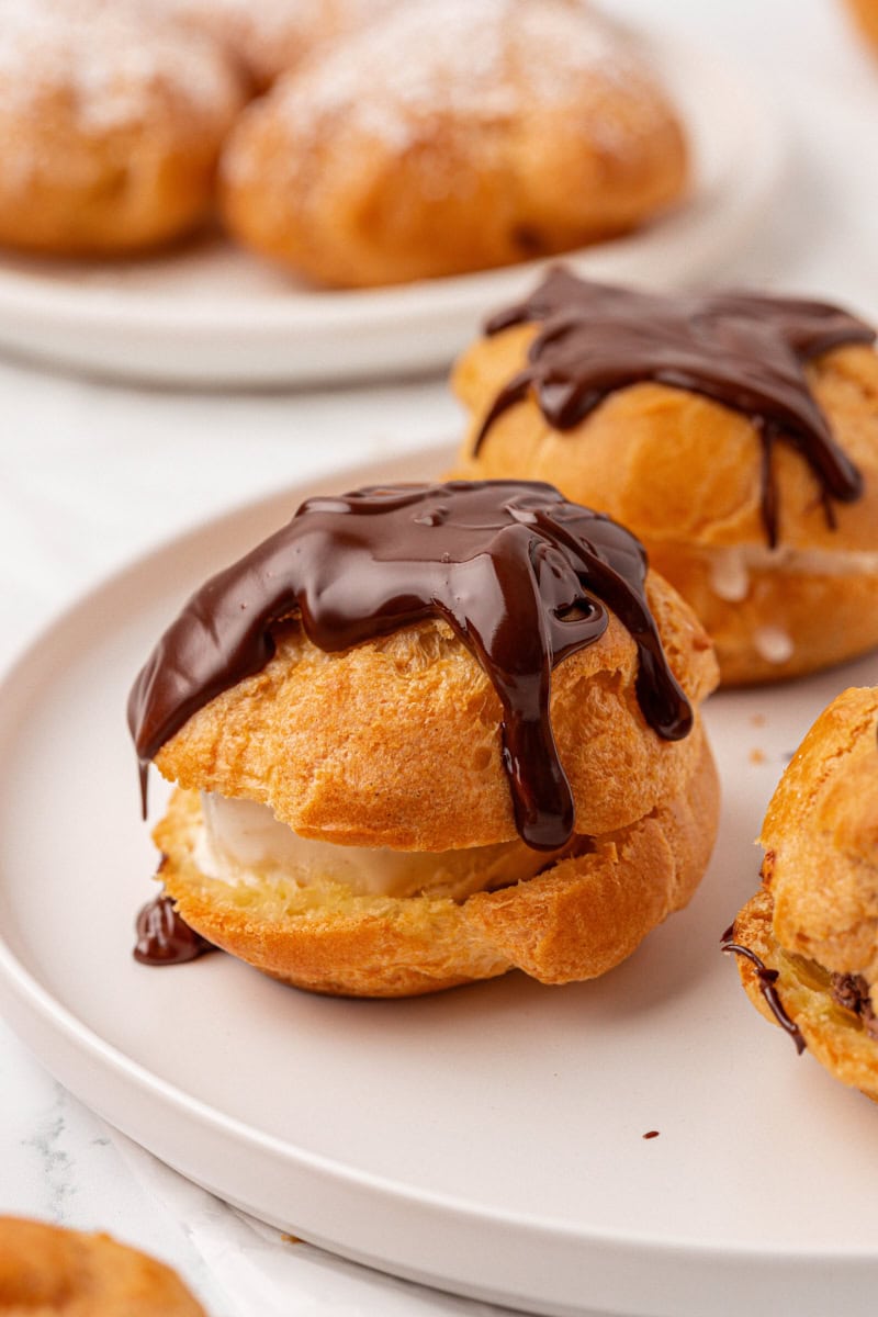 a profiterole filled with vanilla ice cream and topped with chocolate sauce on a white plate