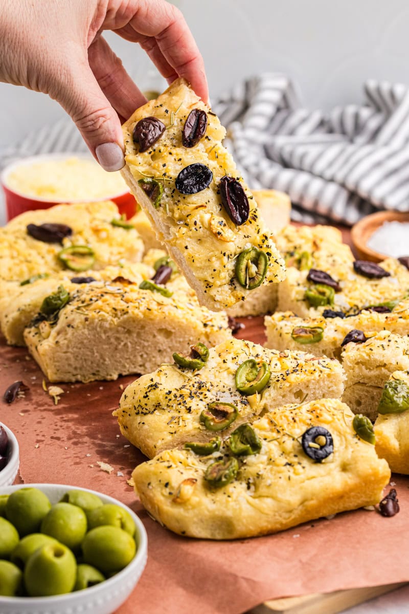 a piece of no-knead focaccia being lifted away from more bread