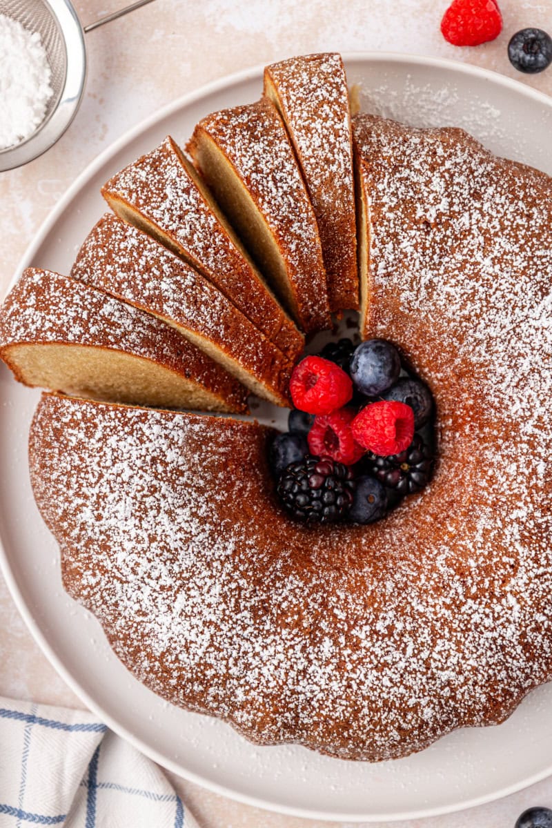 partially sliced buttermilk pound cake topped with powdered sugar and served with fresh berries