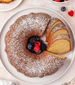 overhead view of partially sliced buttermilk pound cake topped with powdered sugar and served with fresh berries