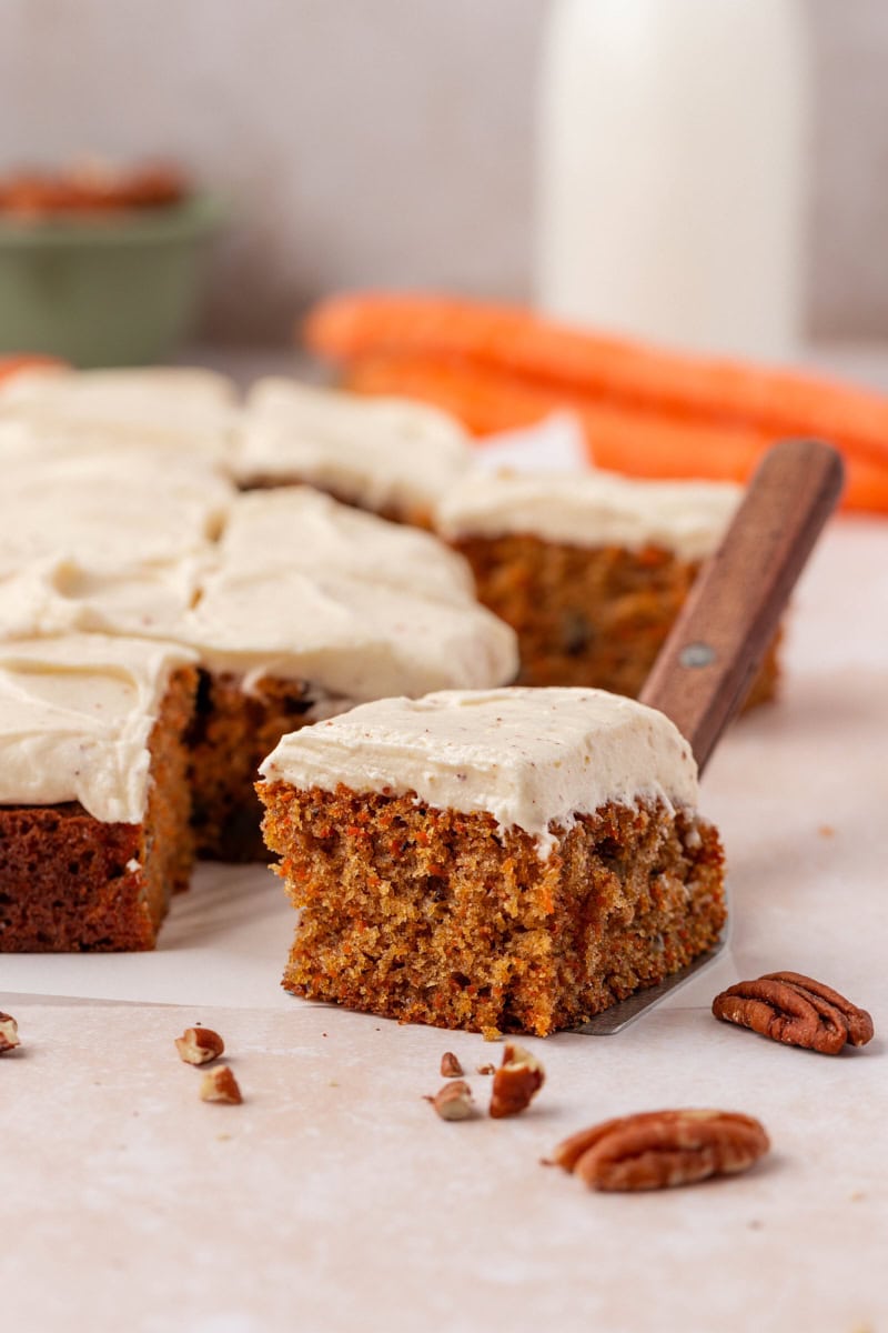 a slice of carrot sheet cake with browned butter cream cheese frosting alongside the remaining cake