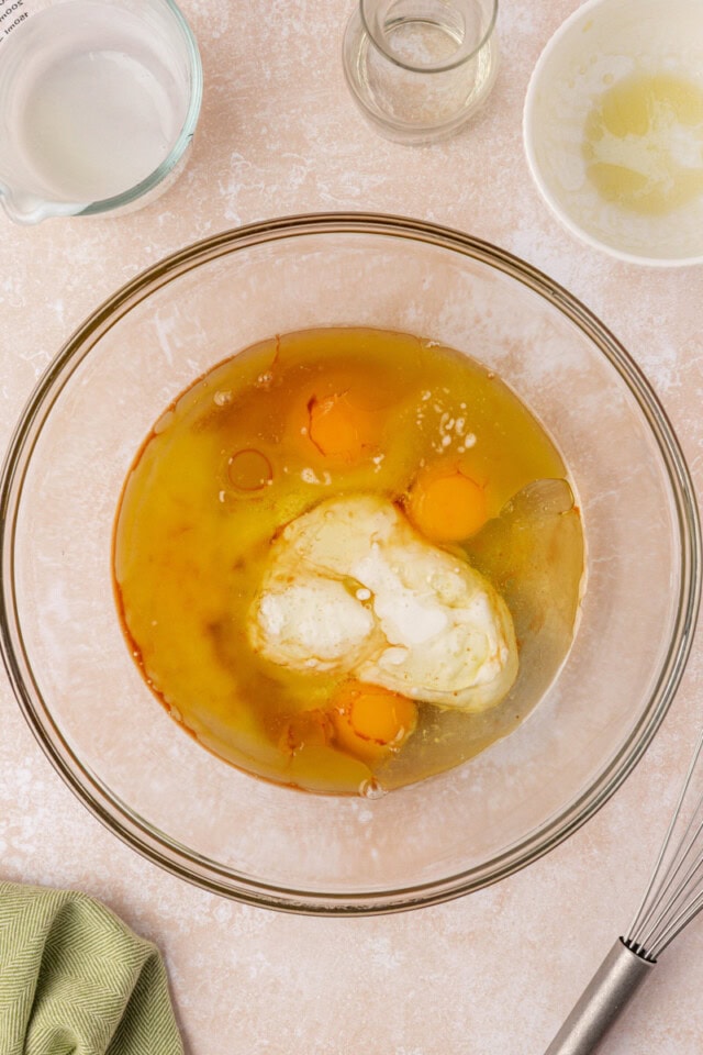 overhead view of eggs, melted butter, oil, buttermilk, and vanilla in a mixing bowl