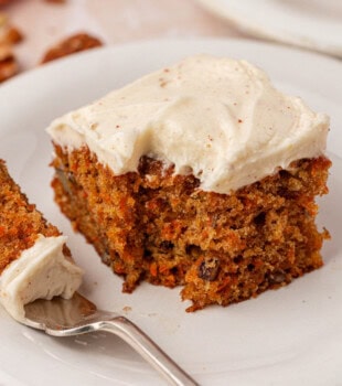 a slice of carrot sheet cake with browned butter cream cheese frosting on a plate with a bite on a fork