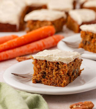 carrot sheet cake with browned butter cream cheese frosting on a white plate with more cake in the background