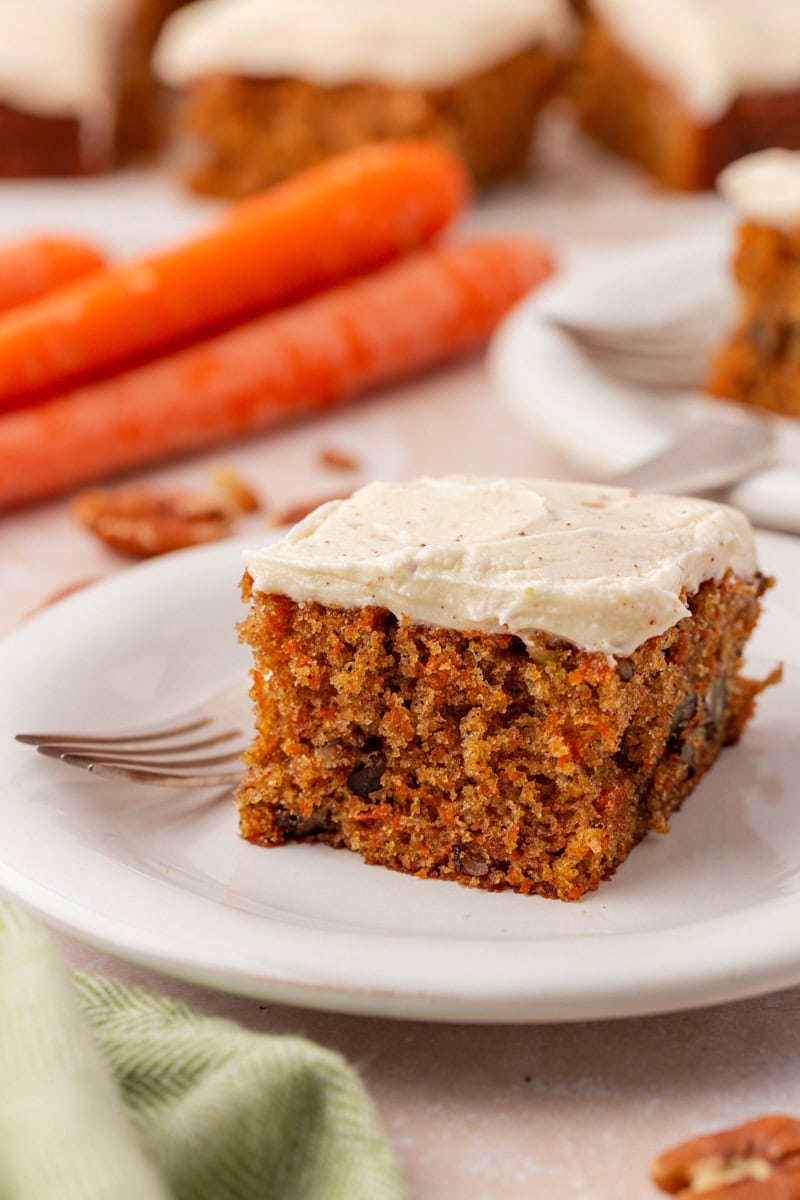 a slice of carrot sheet cake topped with browned butter cream cheese frosting on a white plate