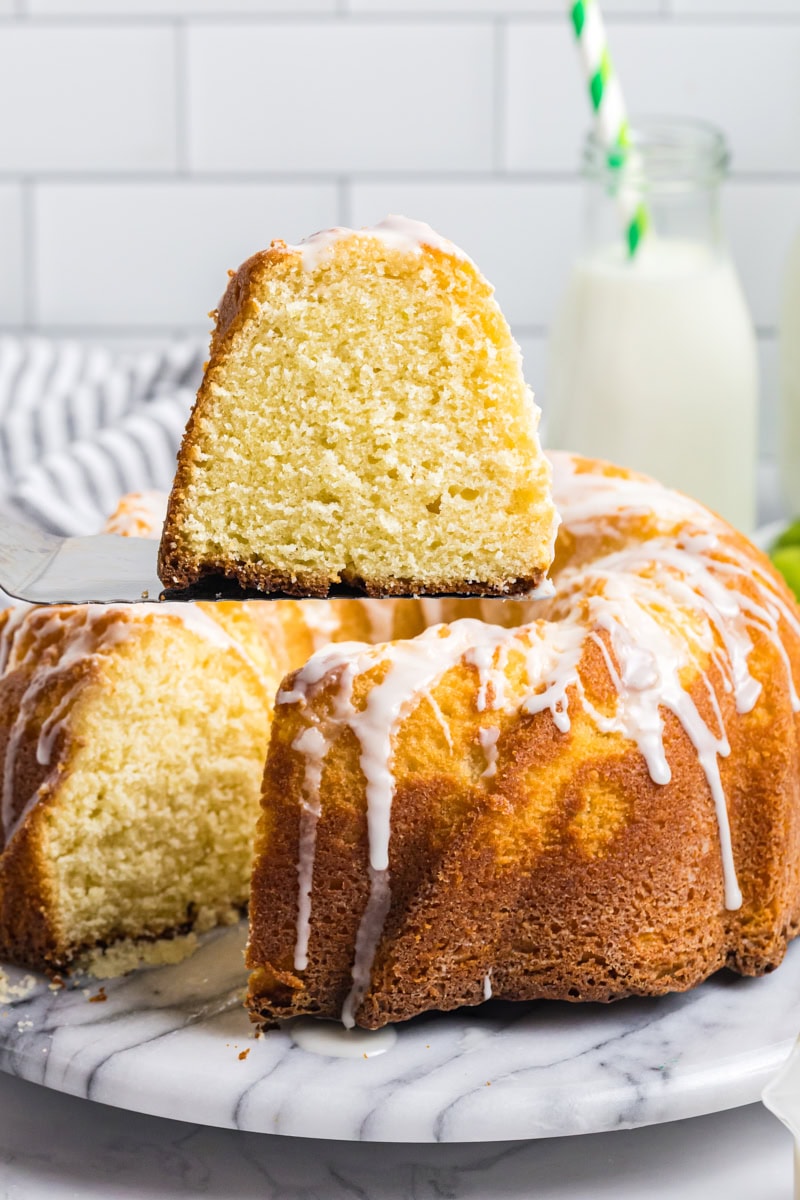 a slice of Key lime Bundt cake on a cake server with the remaining cake in the background