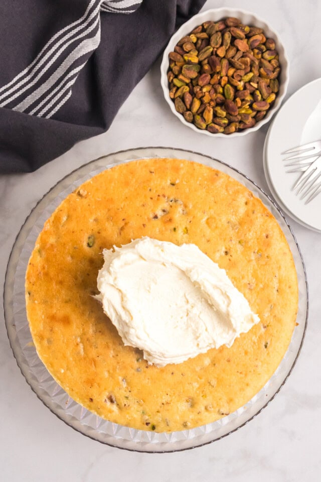 overhead view of white chocolate frosting on top of a pistachio cake layer