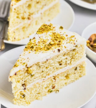 a slice of pistachio cake with white chocolate frosting on a white plate