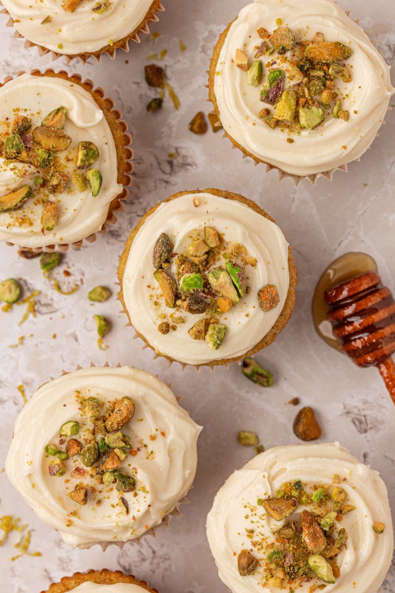 five pistachio cupcakes topped with honey cream cheese frosting and chopped pistachios