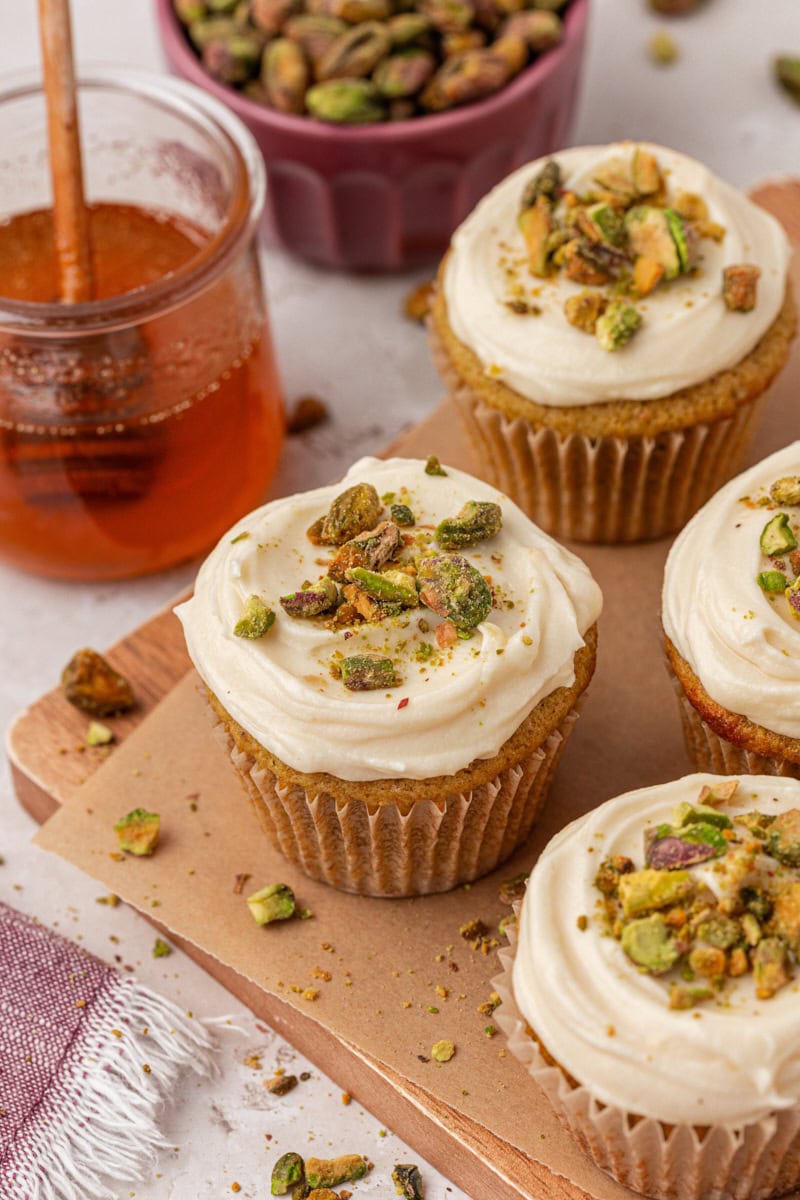 a few pistachio cupcakes with honey cream cheese frosting on a wooden serving board