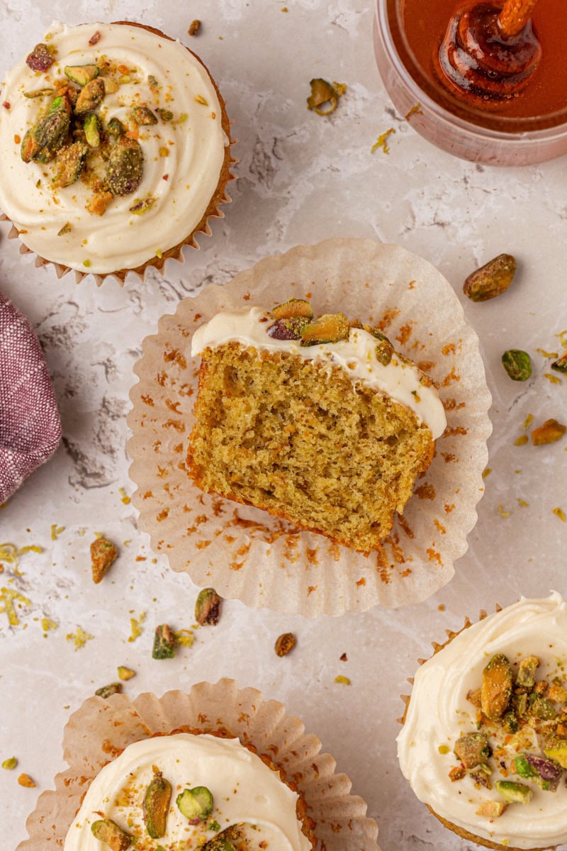 overhead view of half of a pistachio cupcake with. honey cream cheese frosting turned on its side to show the fluffy, nutty texture