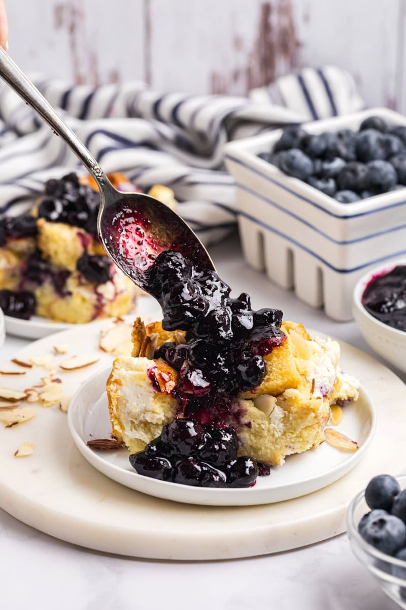 blueberry sauce being spooned over a serving of bread pudding