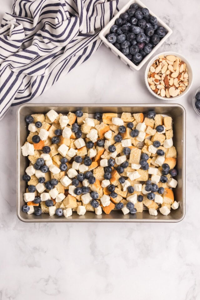 overhead view of cubed stale bread, cream cheese, and blueberries in a 9x13 pan