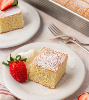 a slice of hot milk cake topped with powdered sugar and served with whipped cream and a fresh strawberry