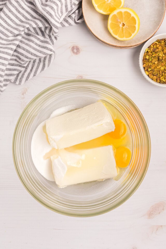 overhead view of cream cheese, sugar, eggs, and lemon juice in a mixing bowl