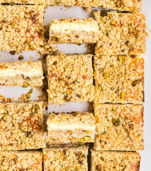 overhead view of sliced lemon pistachio cheesecake bars with a few turned on their sides to show the layers of crust, filling, and crumb