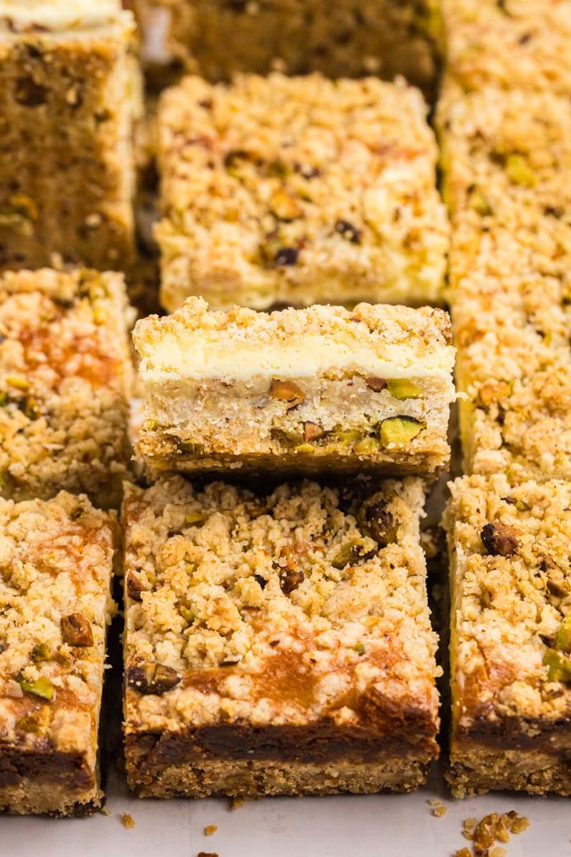 close up of a lemon pistachio cheesecake bar showing layers of pistachio shortbread crust, lemon cheesecake filling, and buttery crumb topping