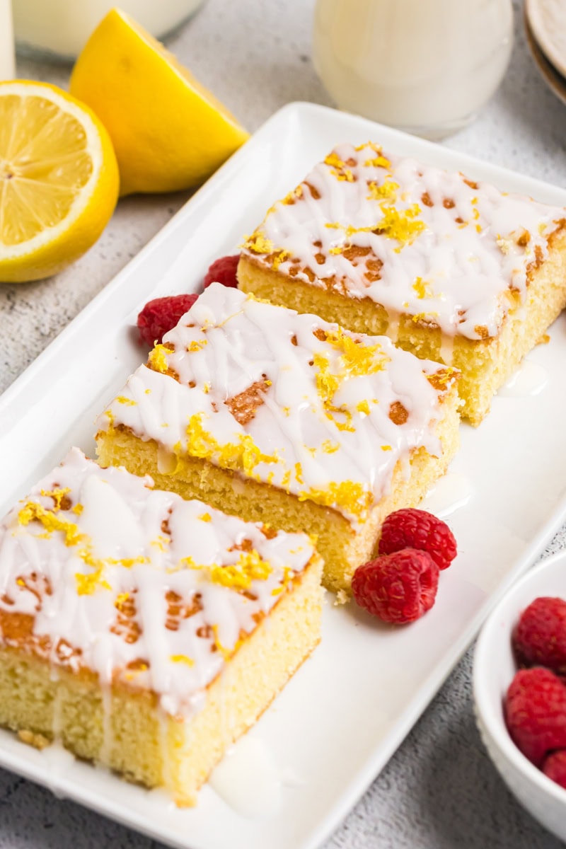 three lemon pound cake bars topped with a lemony glaze and served with fresh raspberries