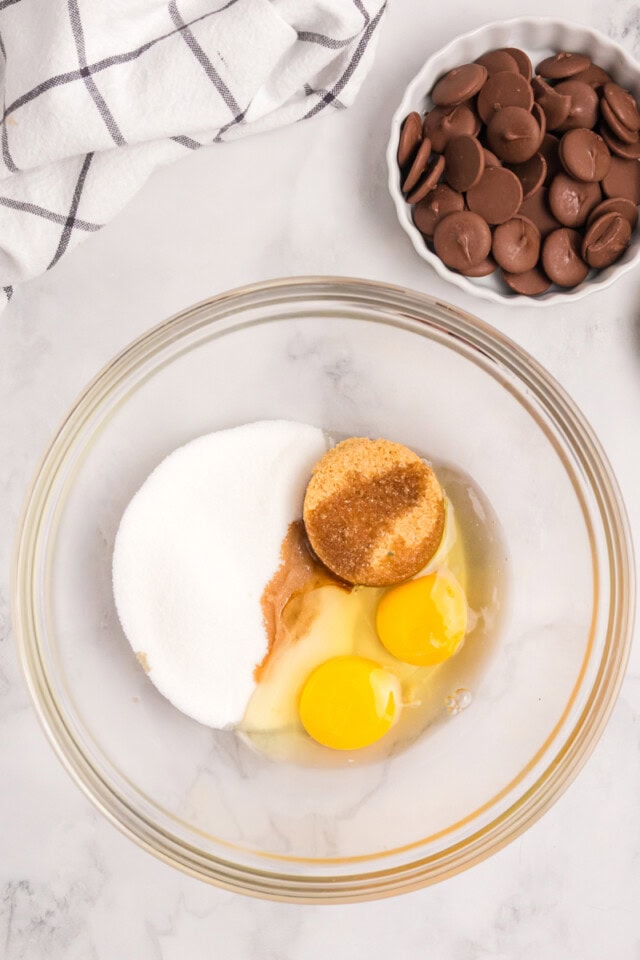 overhead view of sugar, brown sugar, eggs, and vanilla extract in a mixing bowl