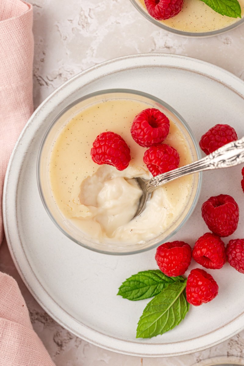 Vue de dessus d'une cuillerée de panna cotta à la gousse de vanille placée sur le reste de la crème anglaise et garnie de baies fraîches