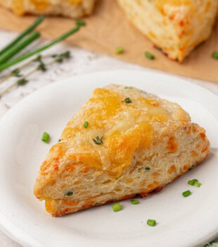 a buttery scone filled with fresh herbs and cheese served on a white plate
