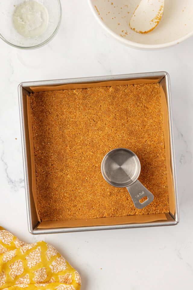 overhead view of graham cracker crust mixture pressed into a square baking pan