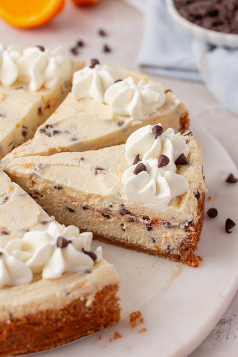 partially sliced cannoli cheesecake topped with whipped cream and mini chocolate chips
