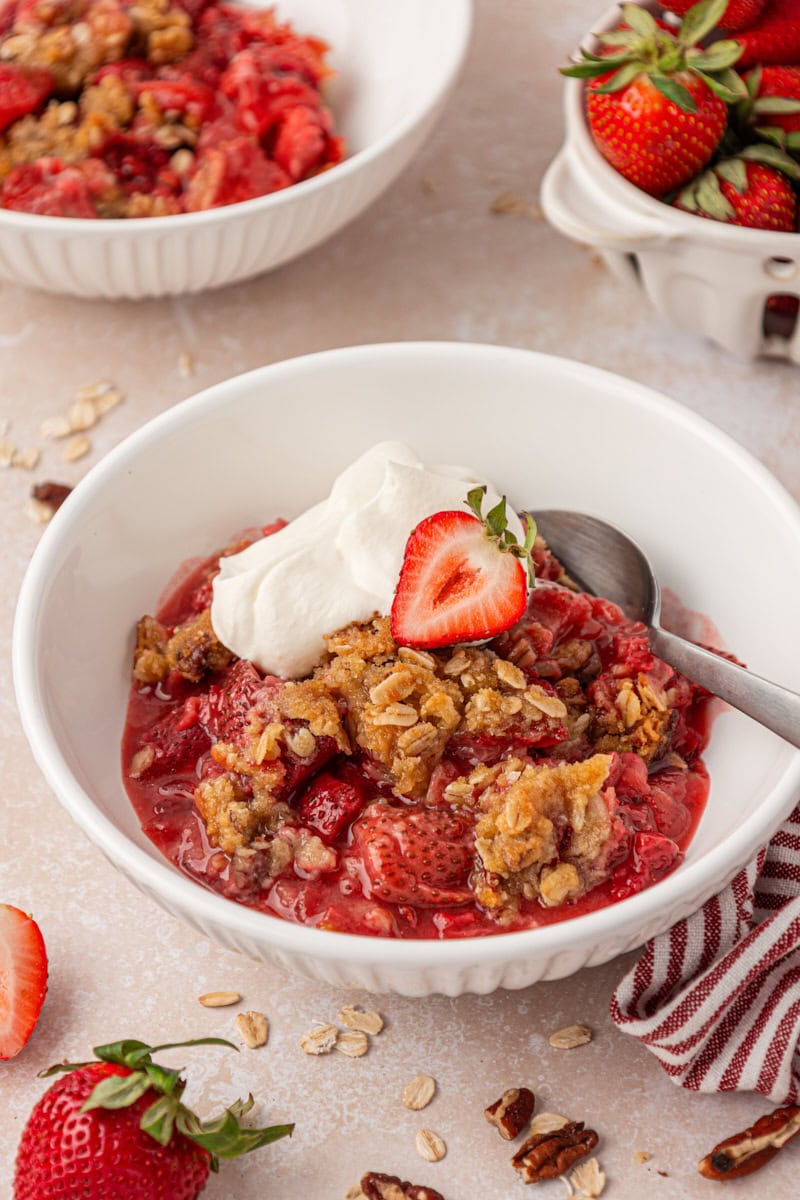 a bowl of strawberry crisp with buttery oat topping served with a dollop of whipped cream