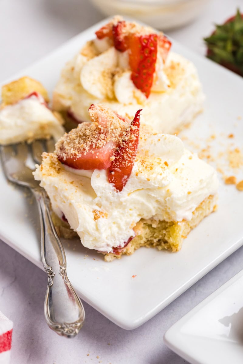 a strawberry shortcake cheesecake bar on a white plate with a bite on a fork