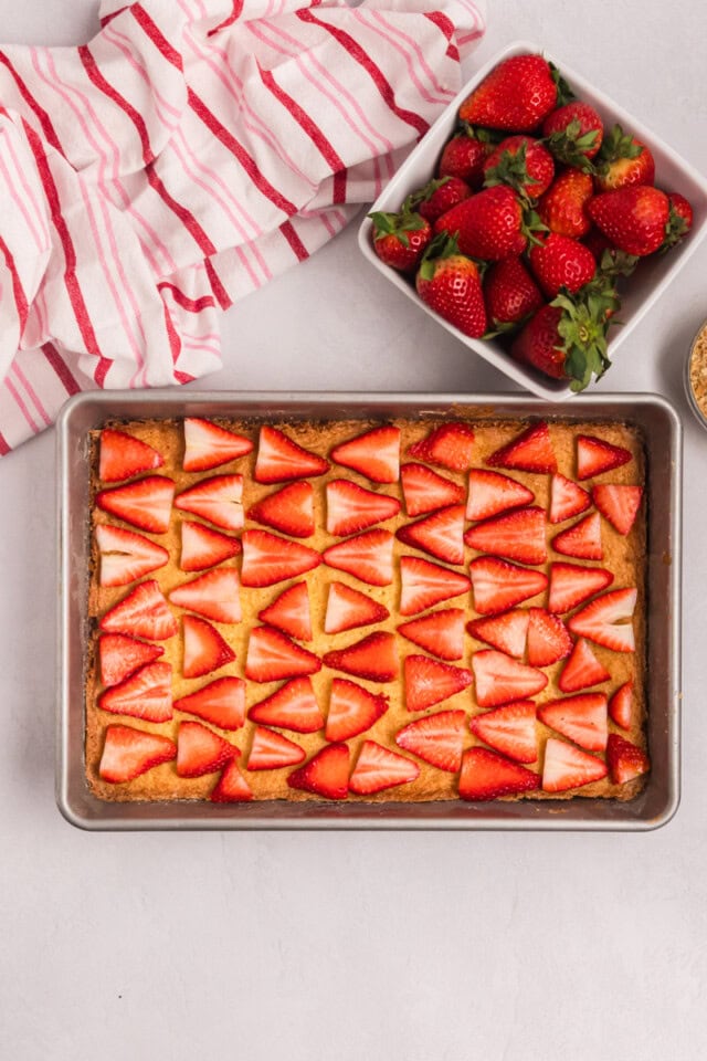 overhead view of sliced strawberries arranged over the top of baked and cooled vanilla cake