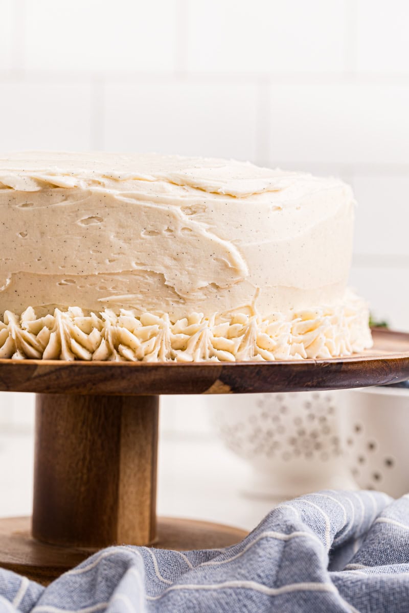 vanilla layer cake frosted with vanilla buttercream on a wooden cake stand